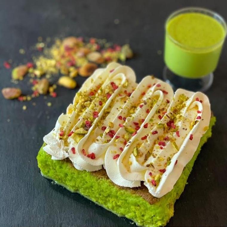 Pistachio milk cake with fresh cream, pistachio crumb and rose, beside a pistachio milkshake