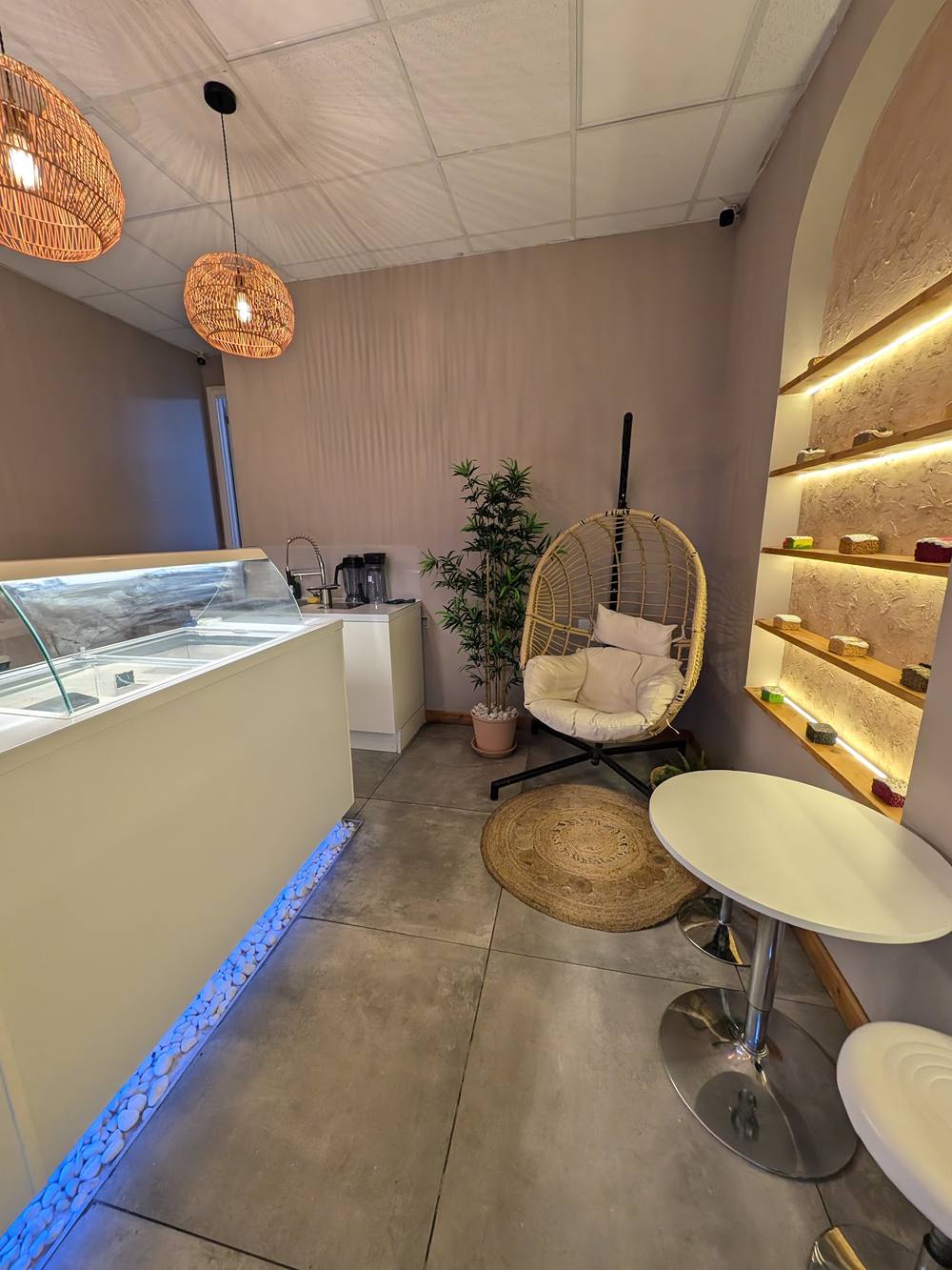 Inside Cakes & Craves — warm rattan pendant lights, a hanging chair and lit wall shelves displaying milk cakes
